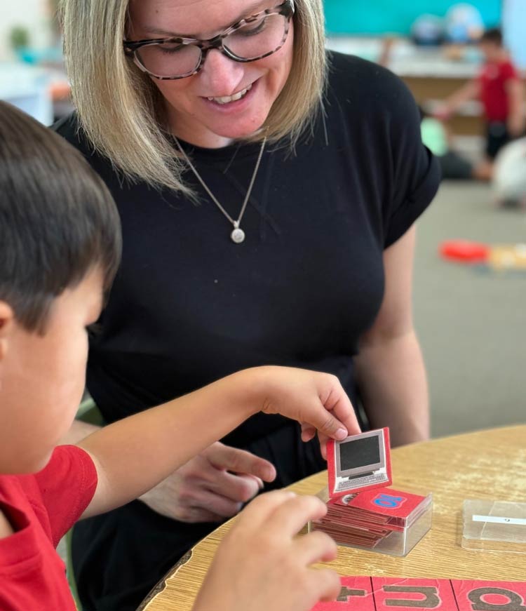A certified Montessori teacher providing individualized instruction to a student using educational learning materials at Greenhouse Montessori School.