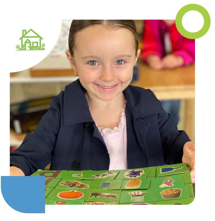 A smiling young student participating in a hands-on Montessori learning activity with illustrated picture cards in a classroom setting.